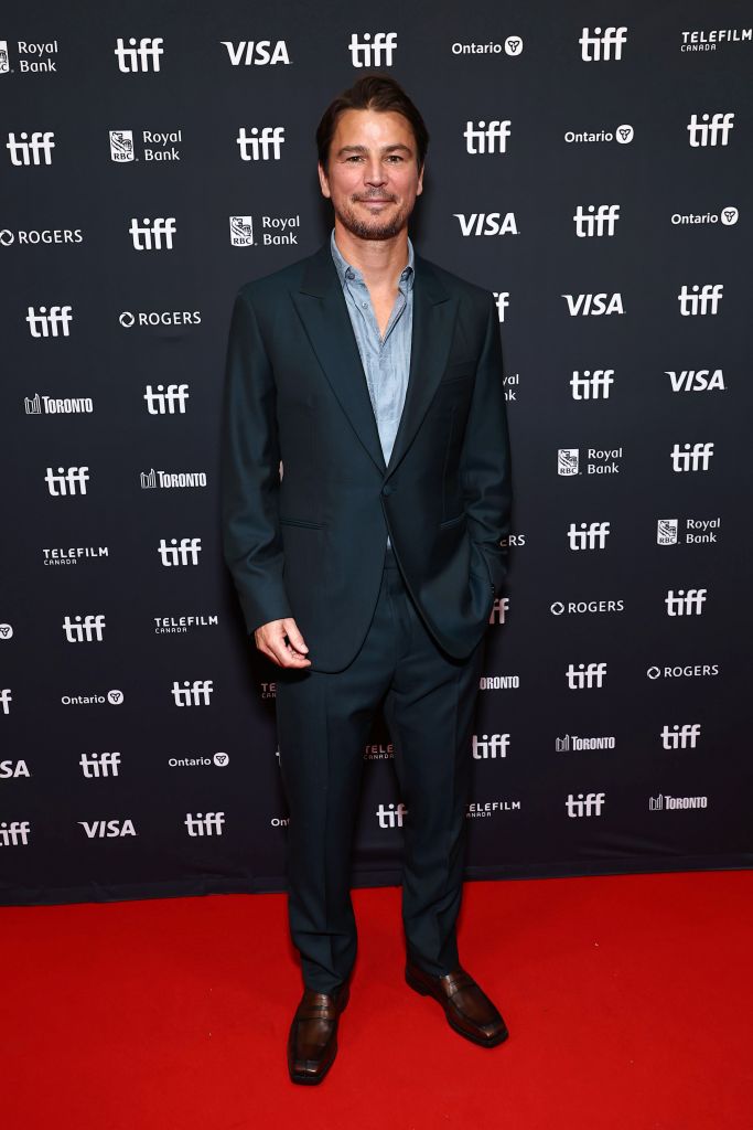 Josh Hartnett poses on a red carpet in a dark suit and light shirt in front of a black backdrop with multiple "TIFF" logos and sponsor logos.