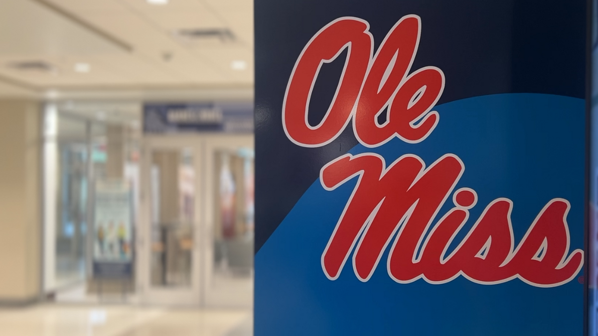 An Ole Miss logo on a wall in the foreground with a blurred building interior behind it.