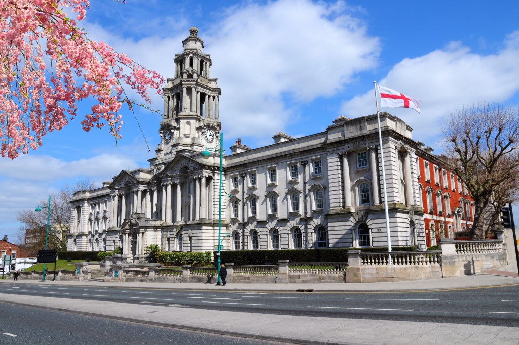 Stockport Town Hall on a sunny day in spring, with pink cherry blossoms in the foreground.