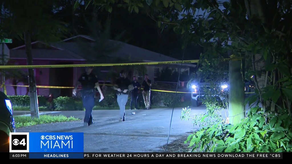 Police officers investigate a crime scene at night, with yellow caution tape marking off the area.