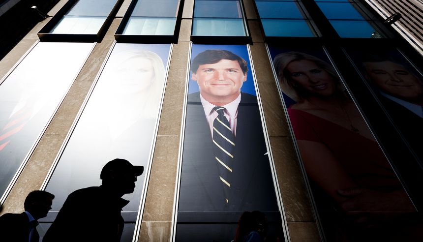 People walk past pictures of Fox News hosts including Tucker Carlson at the studios of Fox News in 2019.