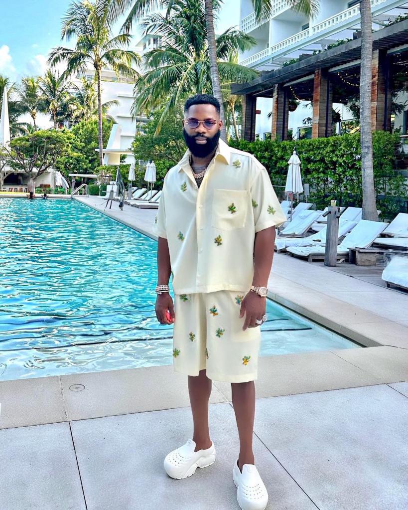 Igho "Tiny" Ubiribo stands by a swimming pool, wearing sunglasses, a light yellow shirt and shorts with leaf patterns, and white shoes.