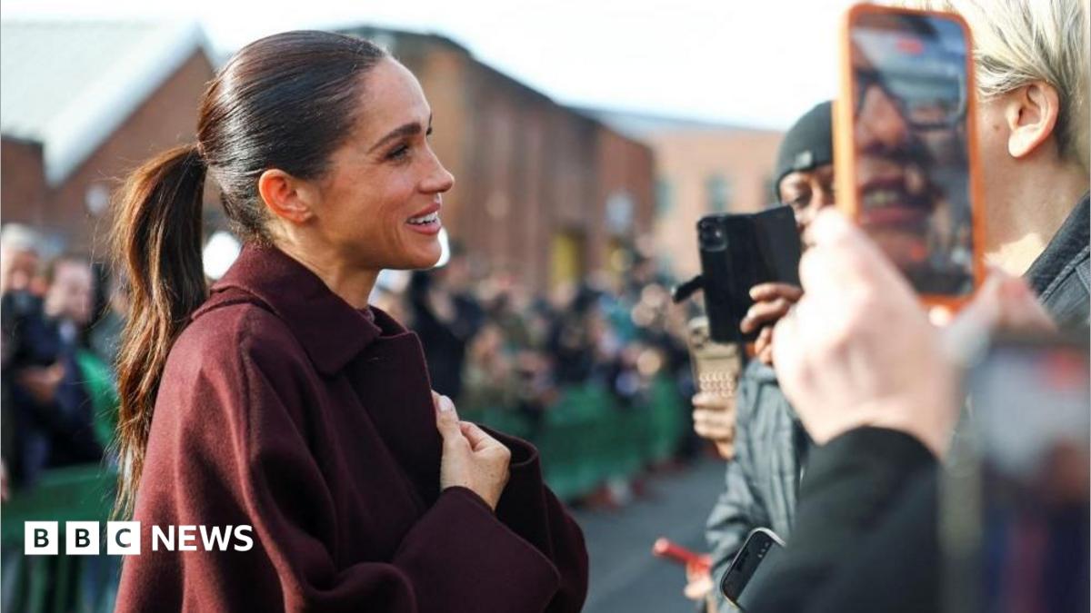 The Duchess of Sussex clutches her hands and smiles warmly as she greets fans waiting for her and Harry in Nottingham