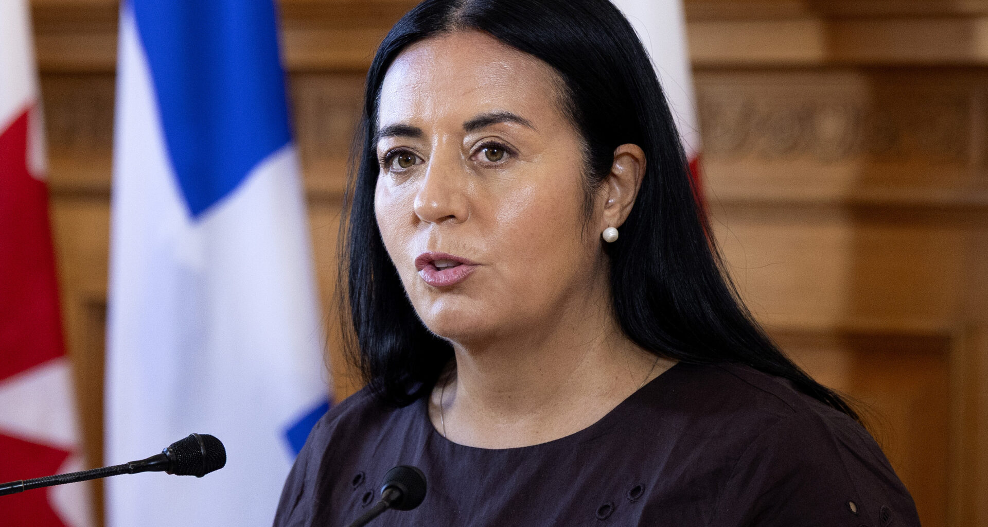 Soraya Martinez Ferrada speaks at a microphone in front of Montreal, Quebec and Canadian flags.