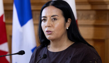 Soraya Martinez Ferrada speaks at a microphone in front of Montreal, Quebec and Canadian flags.