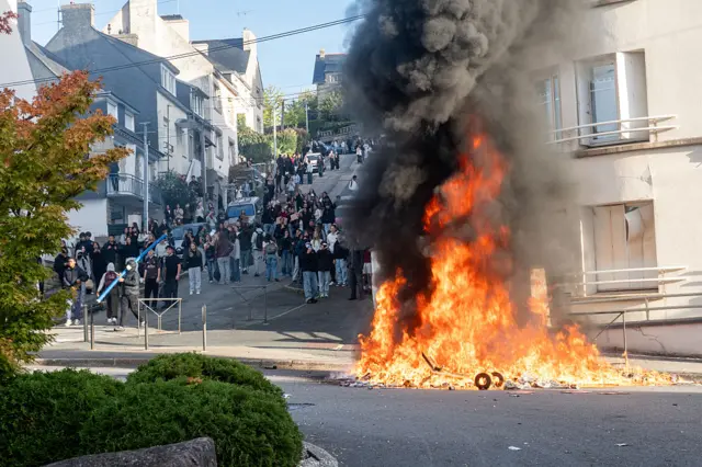 A huge fire at the bottom of the hill as young people gather and look on