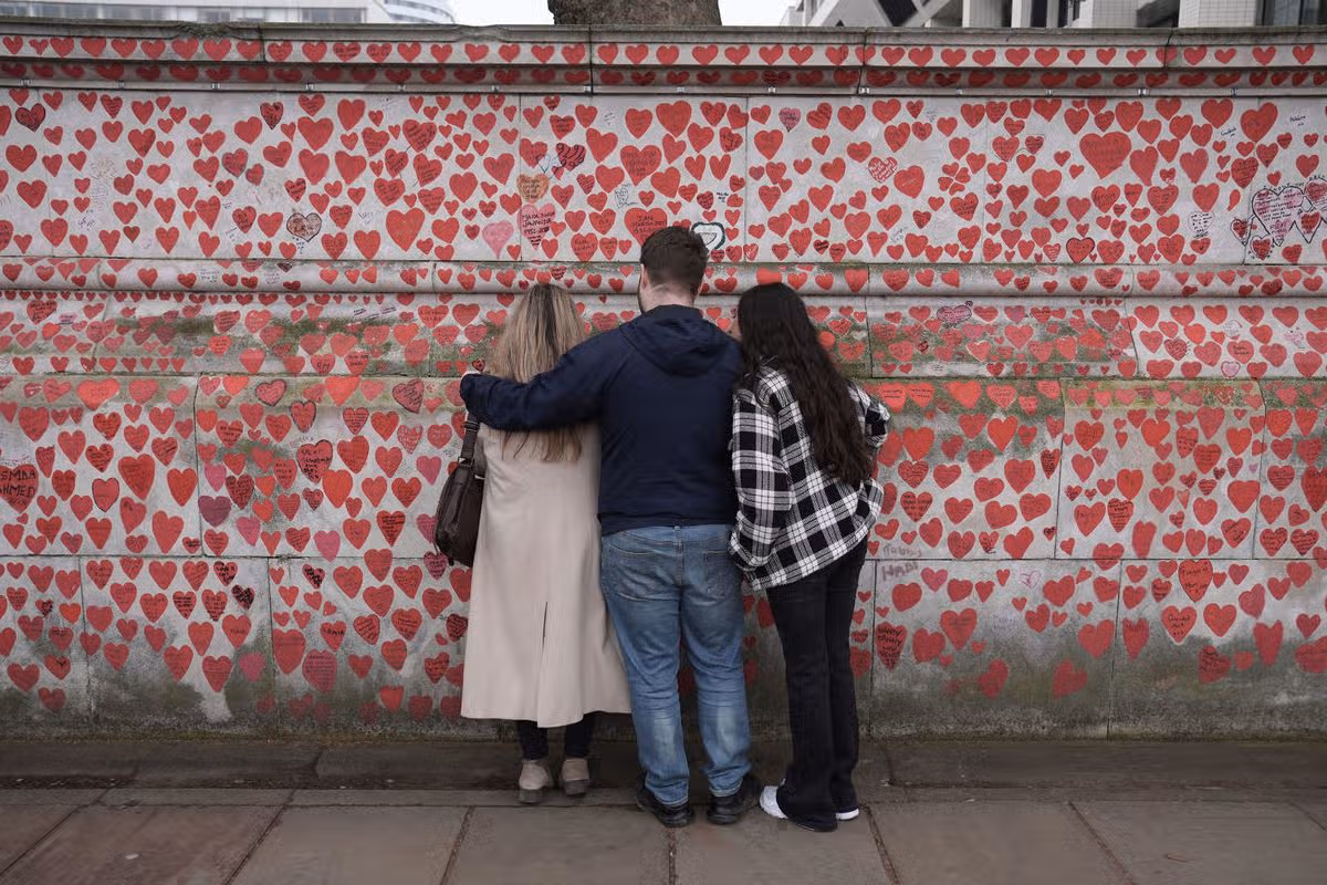 A group of people comfort each other during a service at the National Covid Memorial Wall in London during the annual national Covid-19 day of reflection