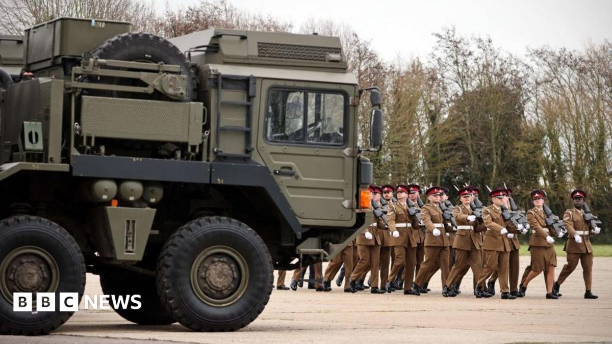 Troops march eyes right next to an Army vehicle.