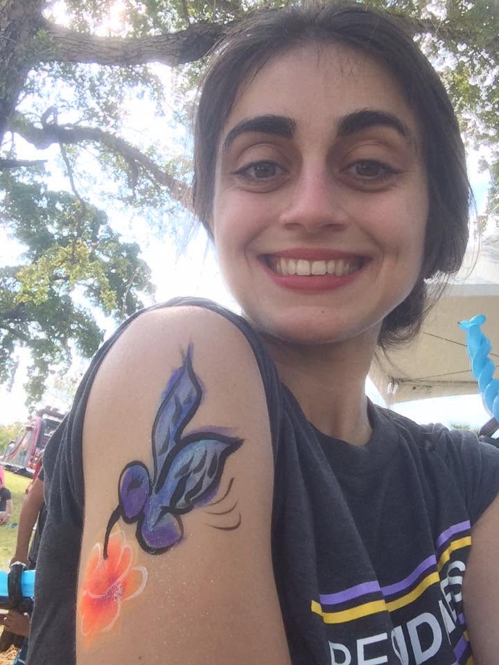 Michelle Alejandra Rubio Leiva smiling outdoors, showing a purple hummingbird painted on her shoulder.
