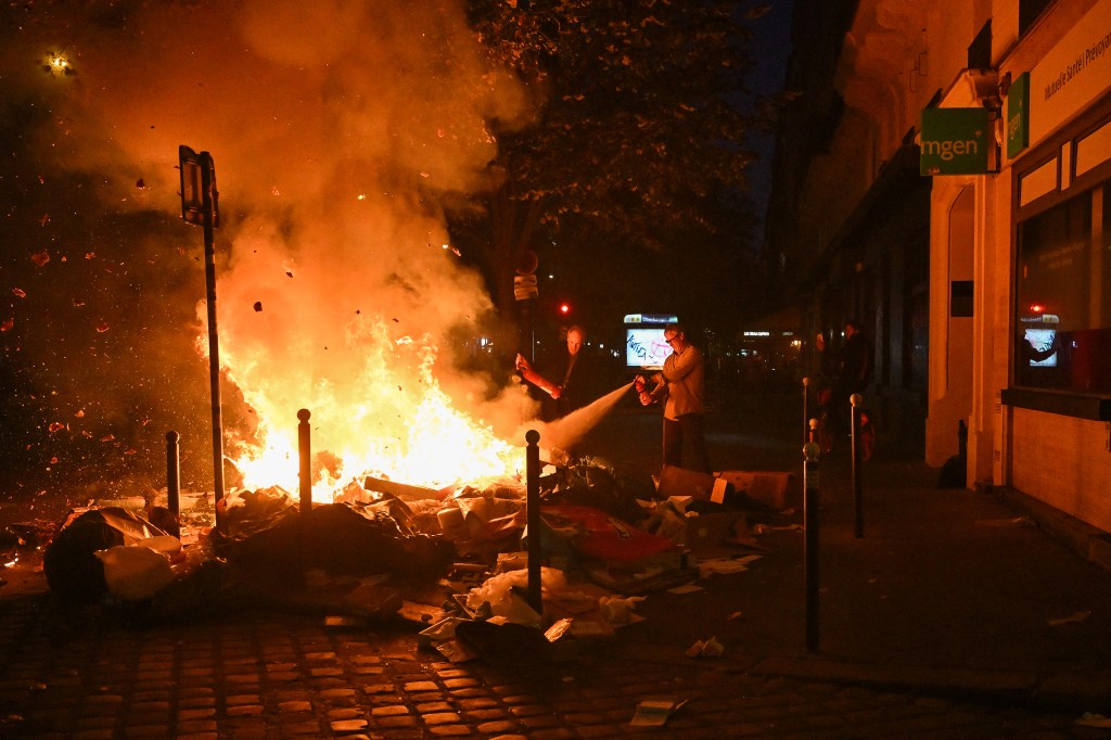 Inhabitants use a fire extinguisher on a burning pile of trash on a street in Paris.