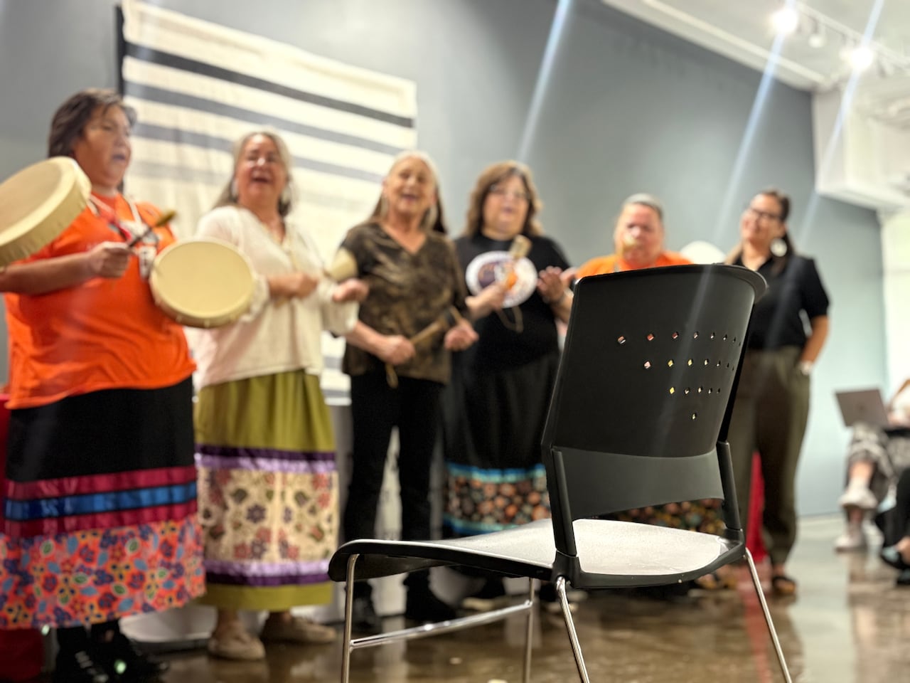 Women singing stand in front of empty chair