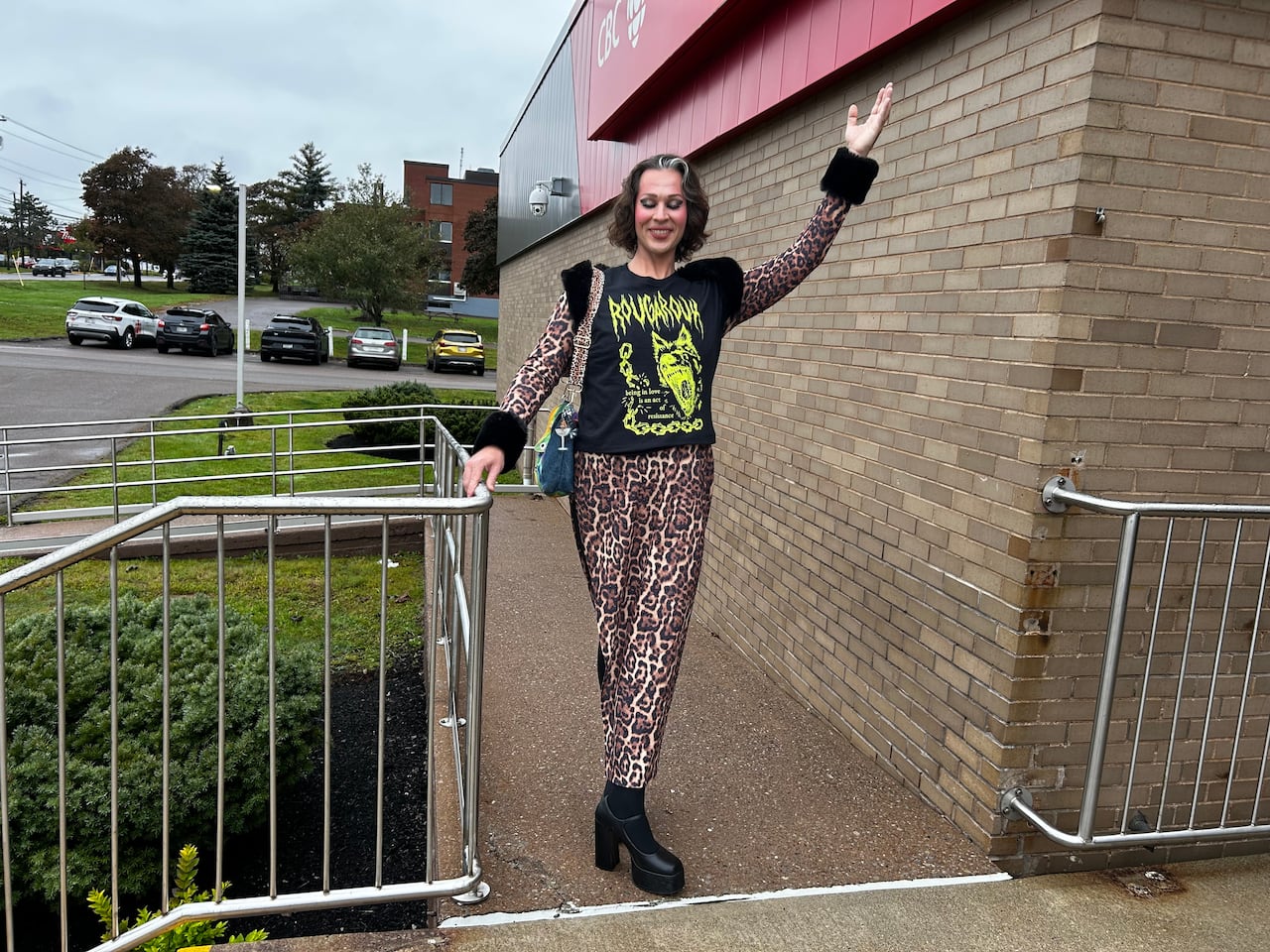 A person in a black shirt and leopard-printed pants stands on a ramp outside a building with red signage.