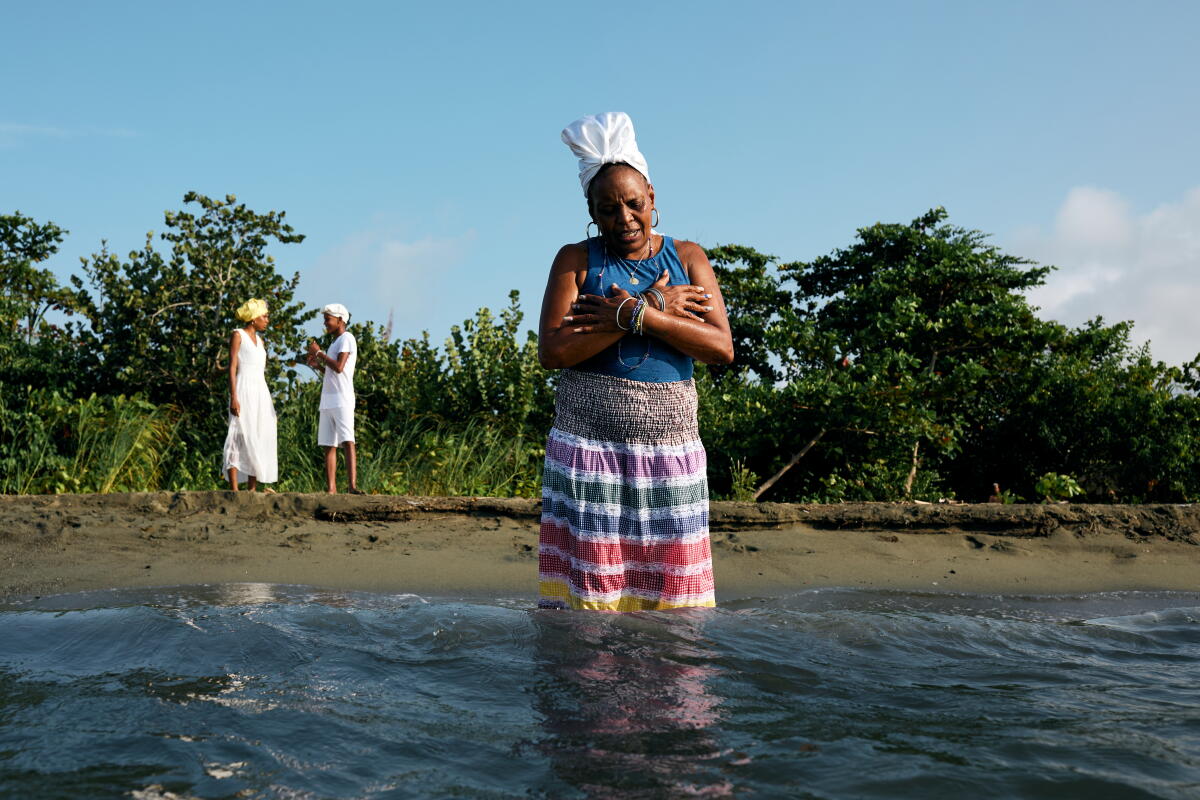a woman stands in the ocean up to her knees as two children stand on the shore