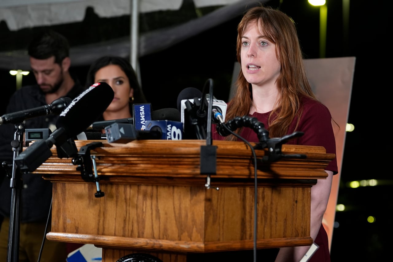 A woman speaks into microphones from behind a wooden podium.