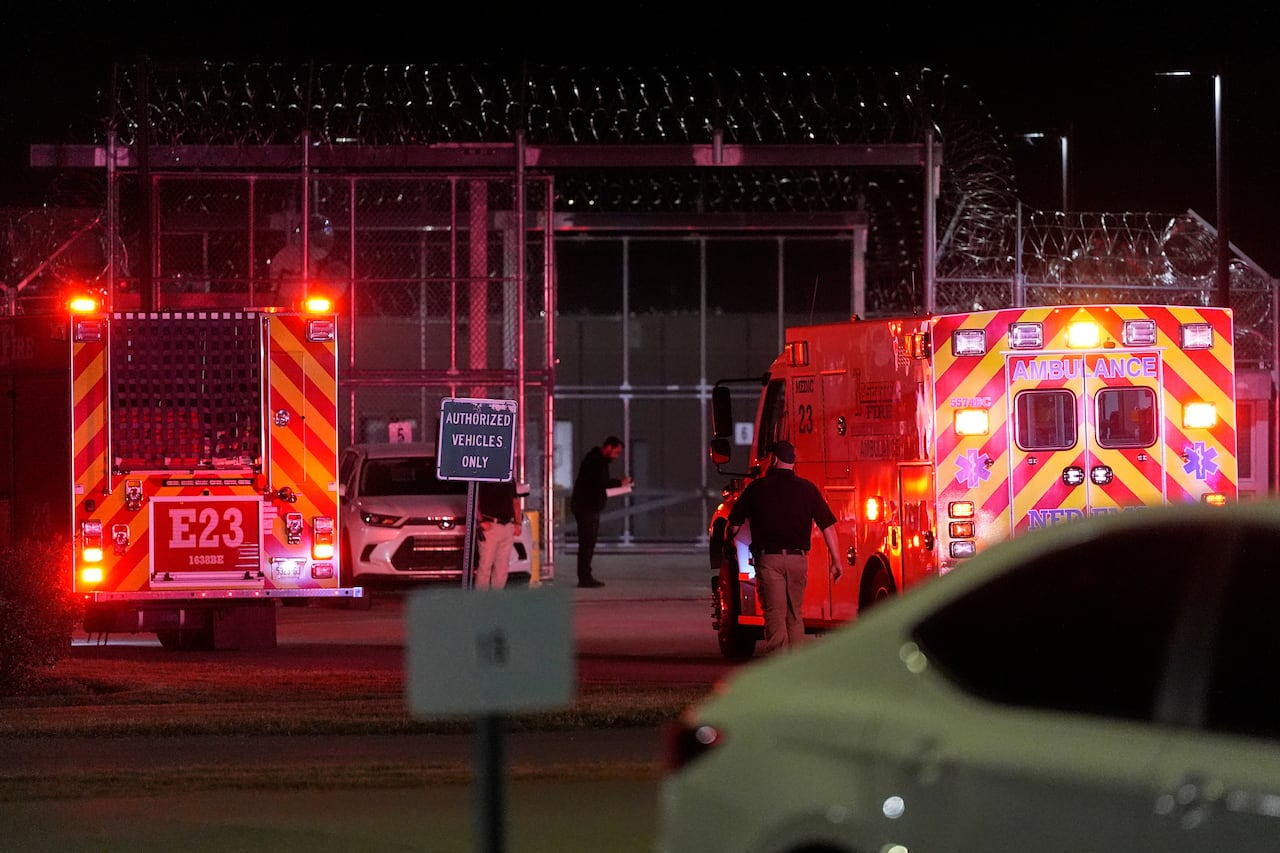 Emergency vehicles with bright red lights are seen in front of a fence with barbed wire at the top of it.
