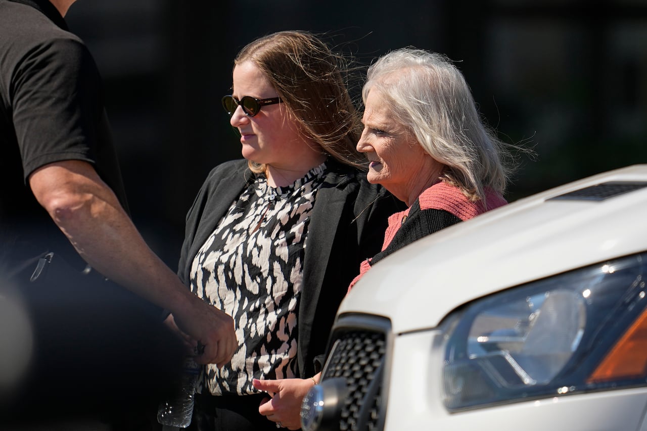 A gray haired woman and a brown haired woman walk past a car
