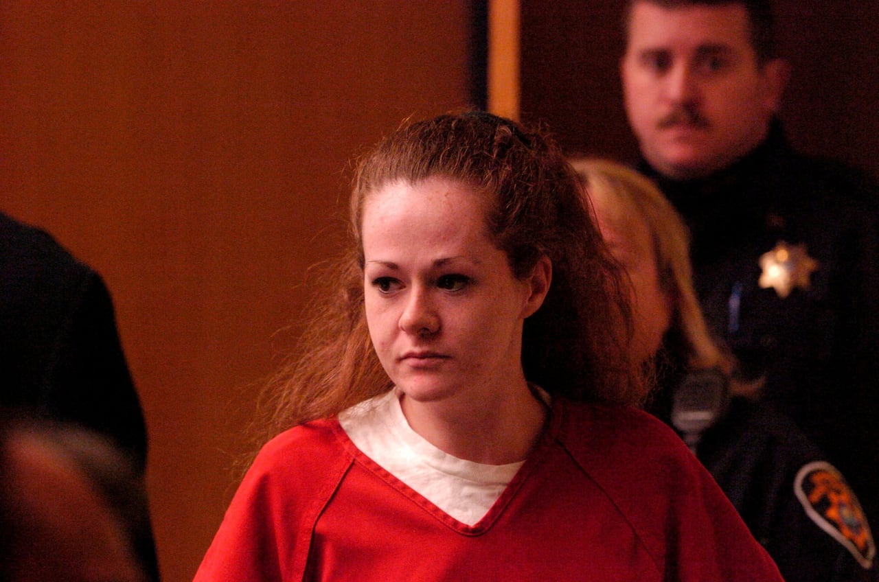 A red-headed woman with a high pony tail wearing bright orange prisons scrubs
