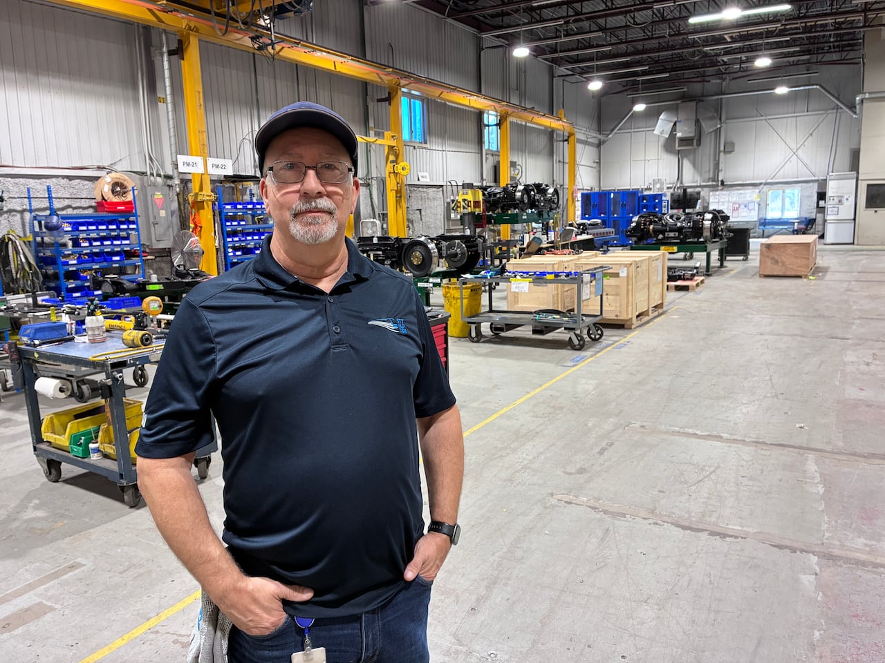 A man in a blue shirt and glasses stands in a warehouse.