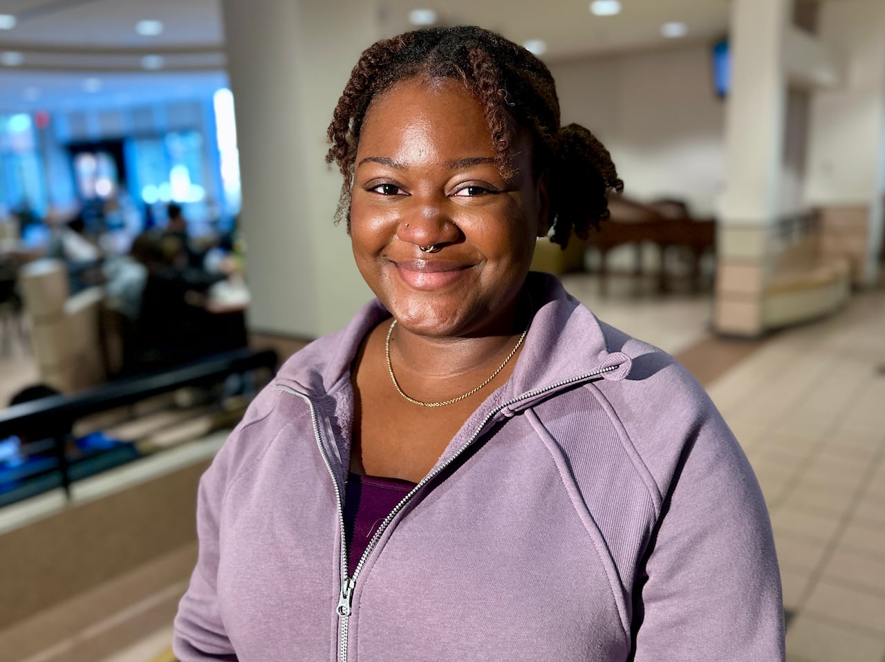 A young woman in a purple hoodies smiles at the camera.
