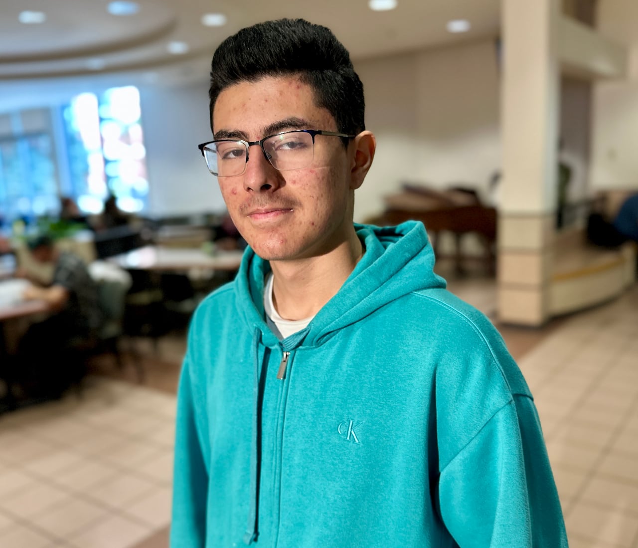 A young man in glasses and a green hoodie smiles at the camera.