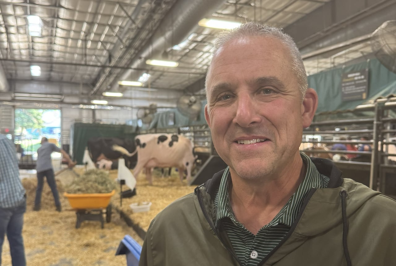 A man poses for a photo with cows and hay in the background.