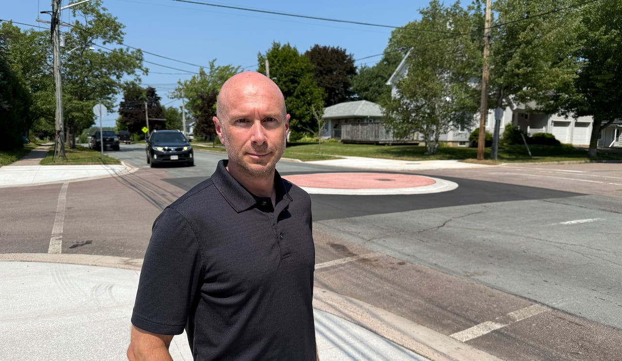 A man in a black polo shirt beside a four-way intersection with a raised red coloured middle section.