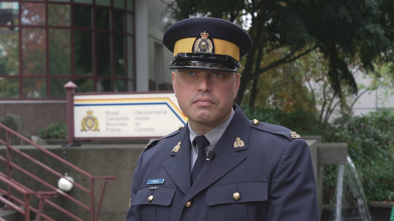 An RCMP officer in a blue uniform in front of an RCMP detachment.
