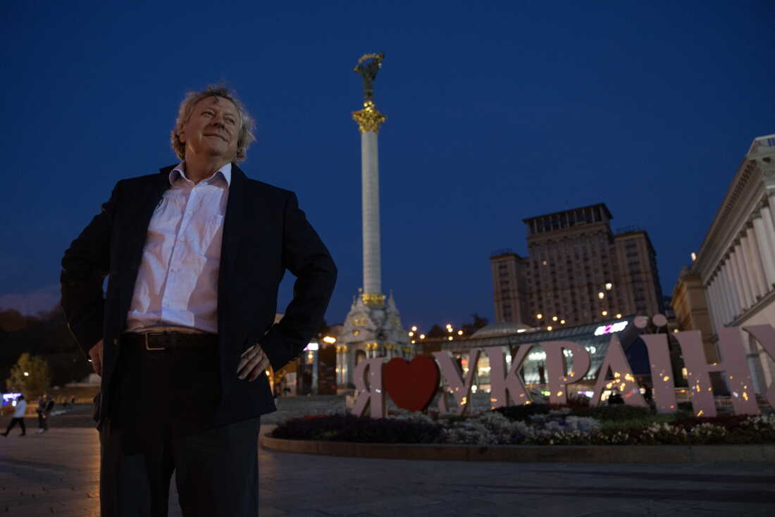 Stephen Humphreys, seen at night in Kyiv in 2024, stands in front of a sign that says in Ukrainian "I heart Ukraine," with a tall monument towering above.