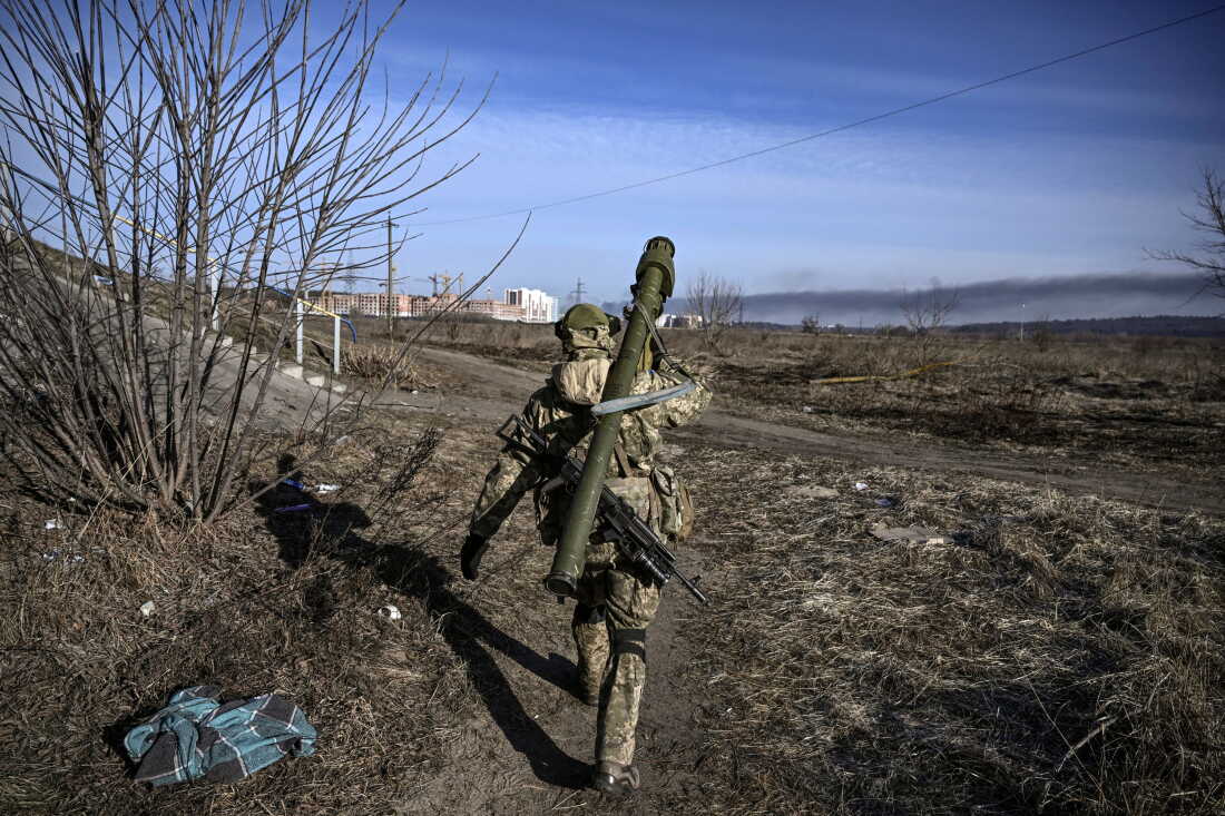 A Ukrainian serviceman wearing a camouflage uniform and carrying firearms slung on his back walks toward the front line in Irpin on March 12, 2022.