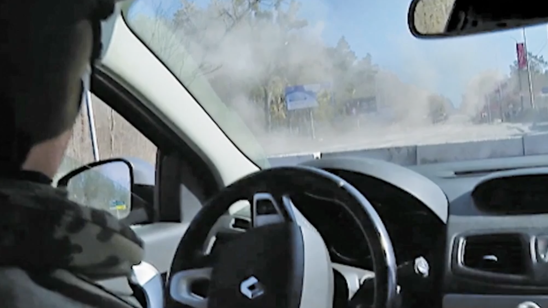 A view from inside the Fox News reporting team's car after a missile hit in front of it. Through the windshield, one can see the road filled with a smoky haze. The car's steering wheel appears at the bottom of the frame.