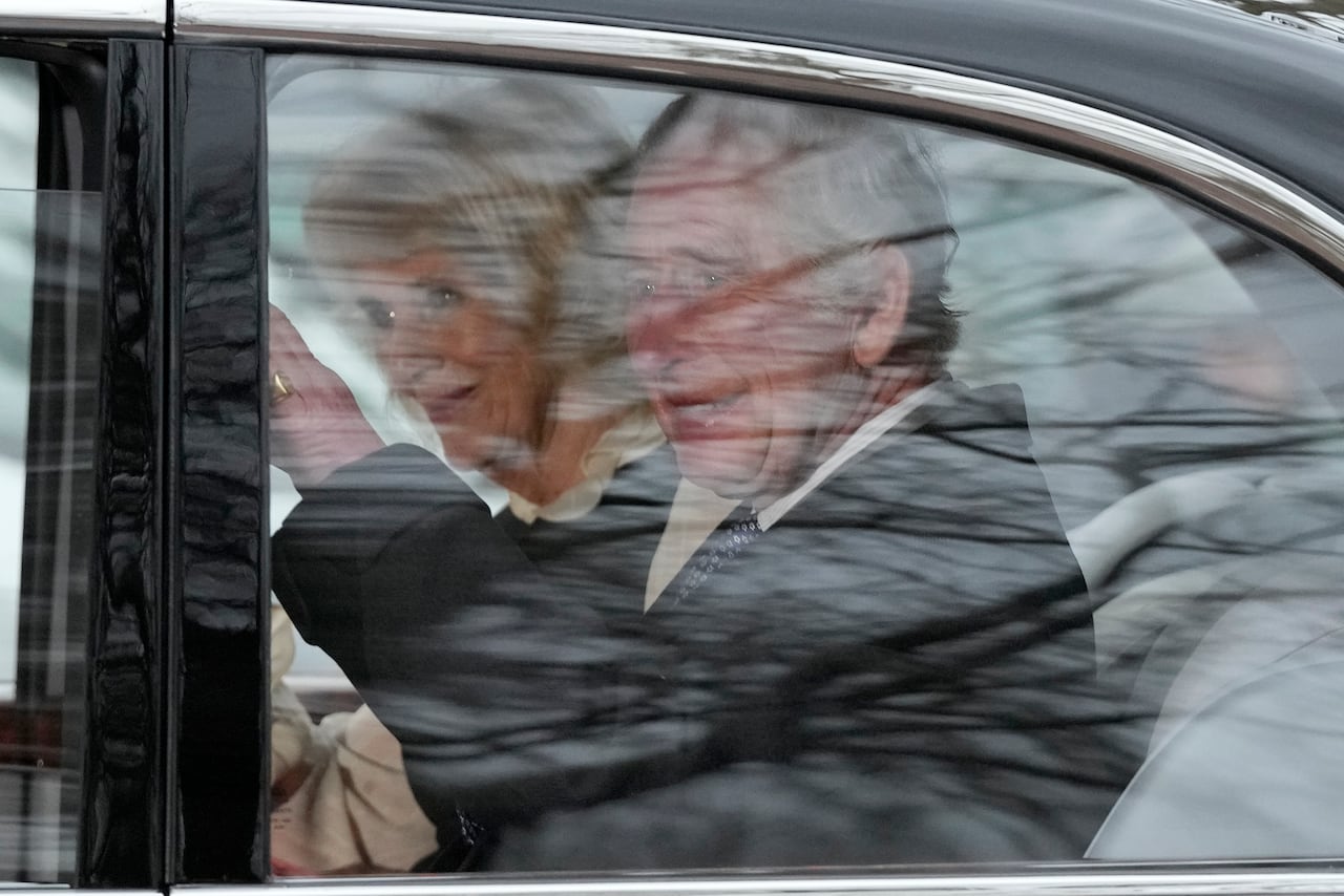 A person sitting in a car waves.