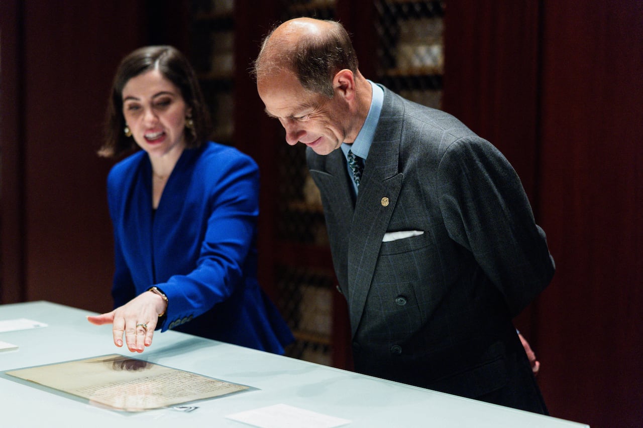 A woman shows a man an archival document in a library. The man looks at the document with interest.