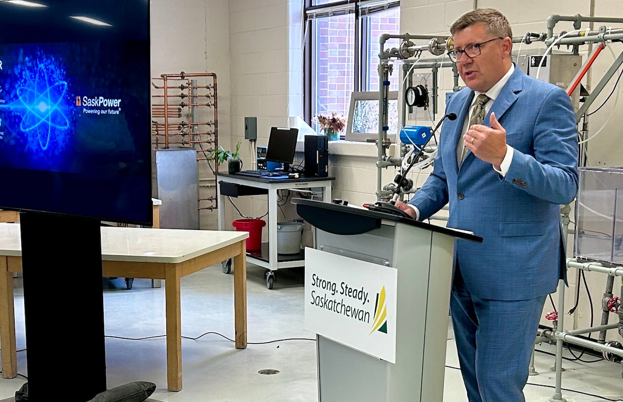 A man in a blue suit stands at a lectern in a laboratory.
