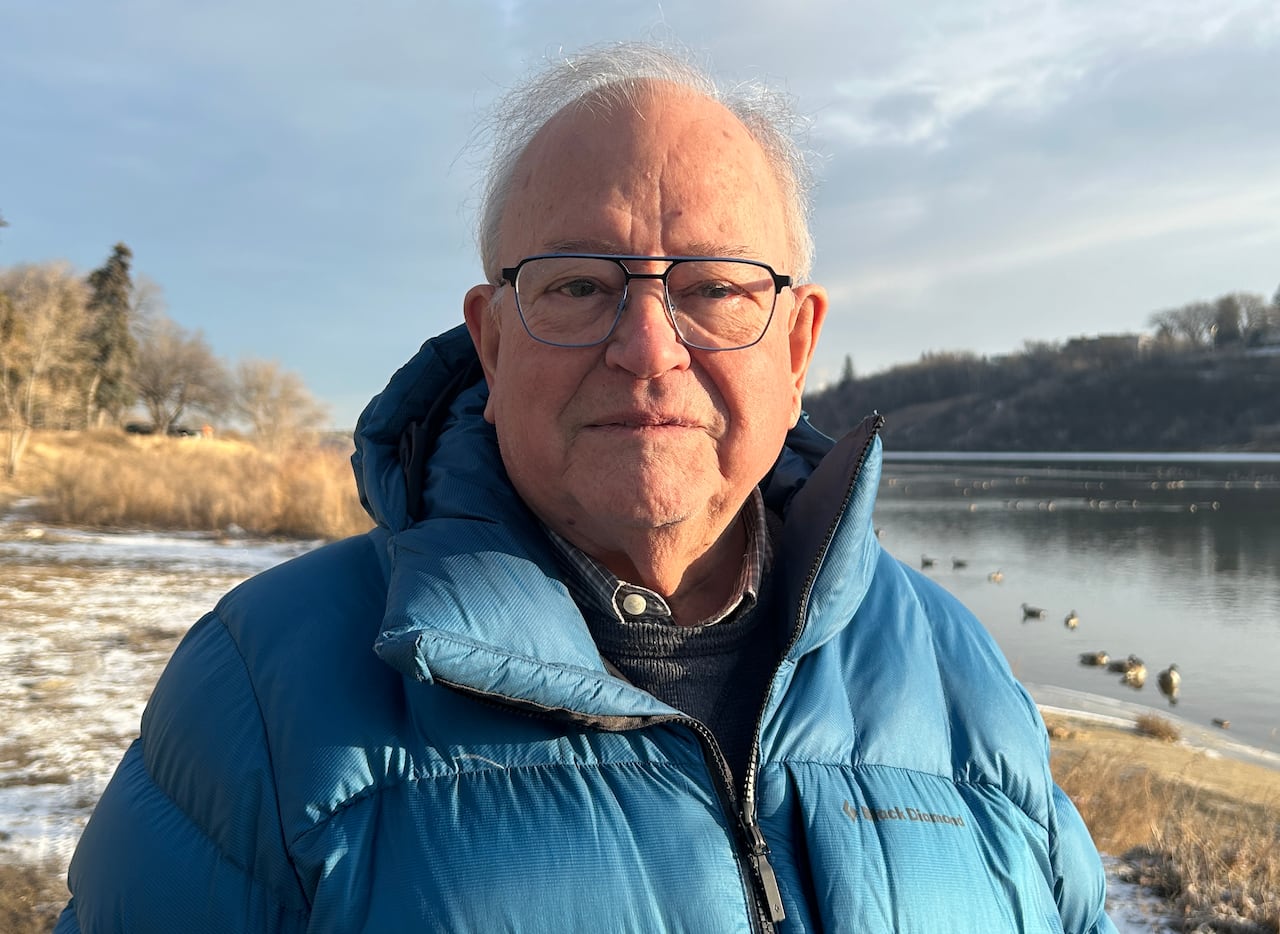 A man in a jacket stands by a river.