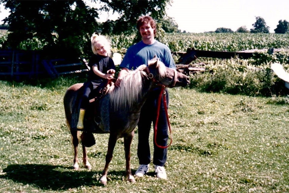 Young child on a horse with a man standing.