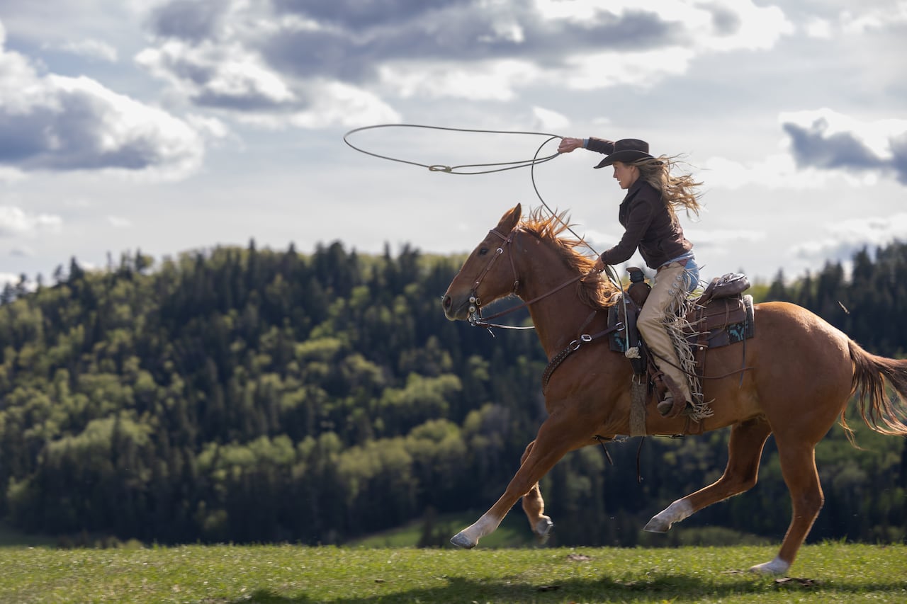 Woman rides a horse while holding lasso.