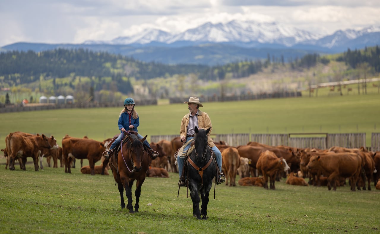 Two people riding horses with the mountains in the background.