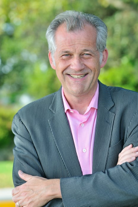Man wearing suit, arms crossed, smiling.