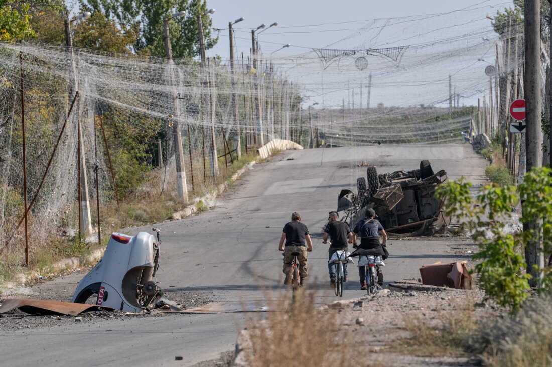 Ukrainian troops ride bikes under an anti-drone net.