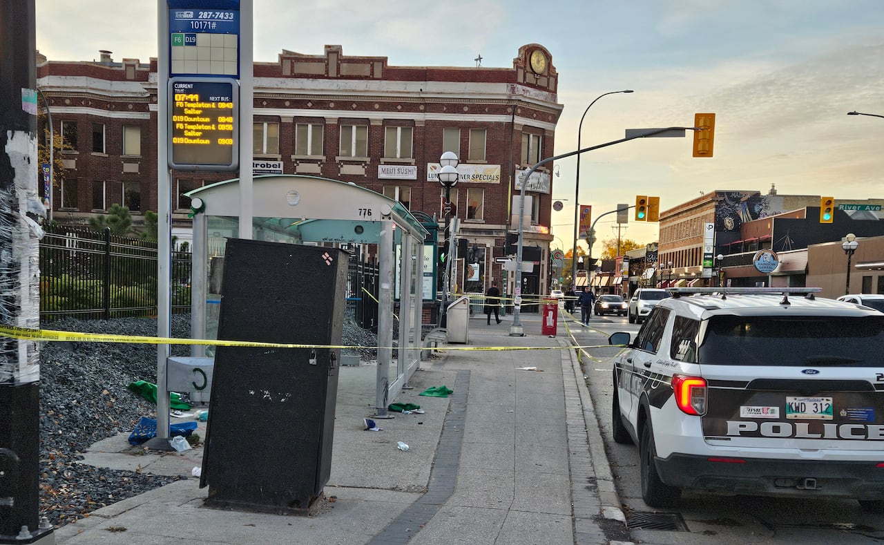Police tape surrounds a street corner and bus shelter. A police cruiser is parked nearby.