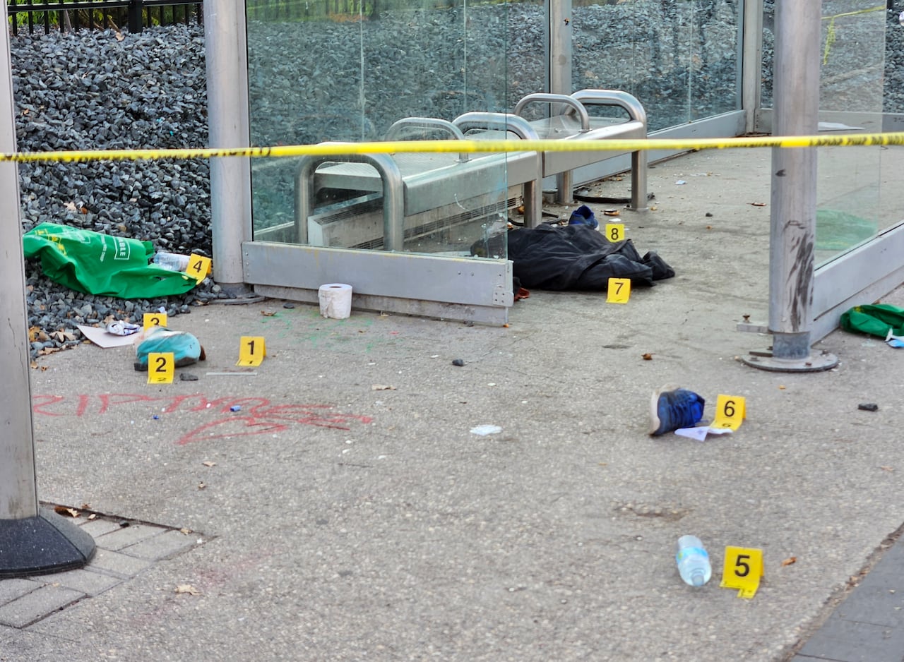 Yellow police evidence tags marks items on the ground inside a bus shelter.