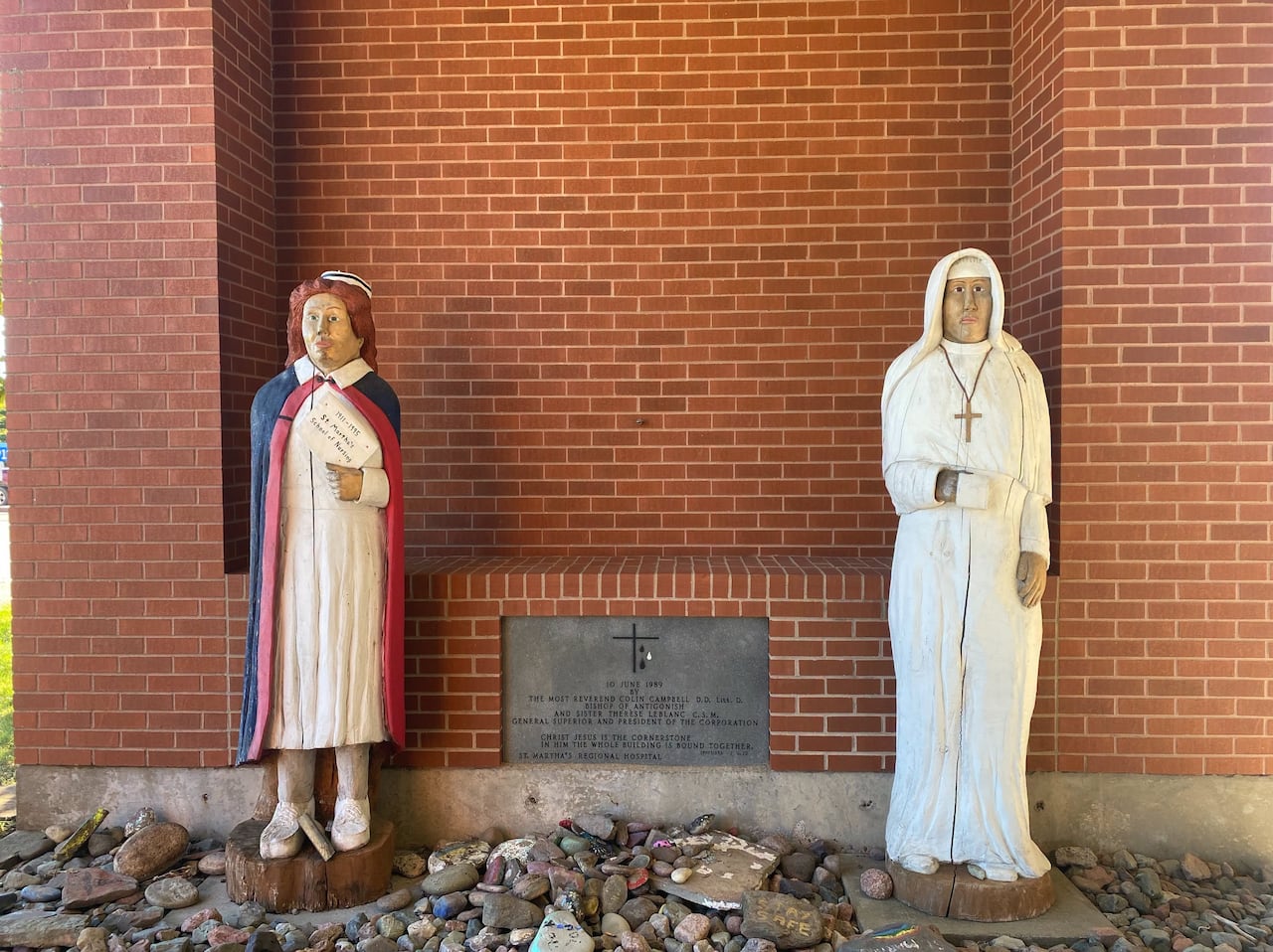 Two statues are seen in front of a brick building. They document a nun and a nursing student.