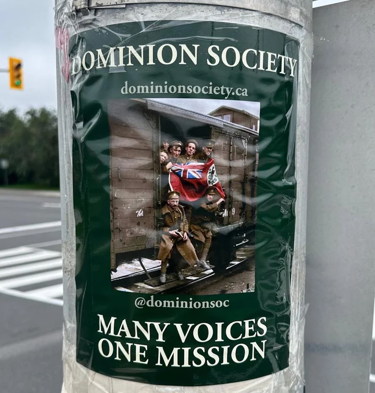 A poster taped onto a utility pole, showing an old image of white men in military uniforms on a train holding the Canadian Red Ensign flag.