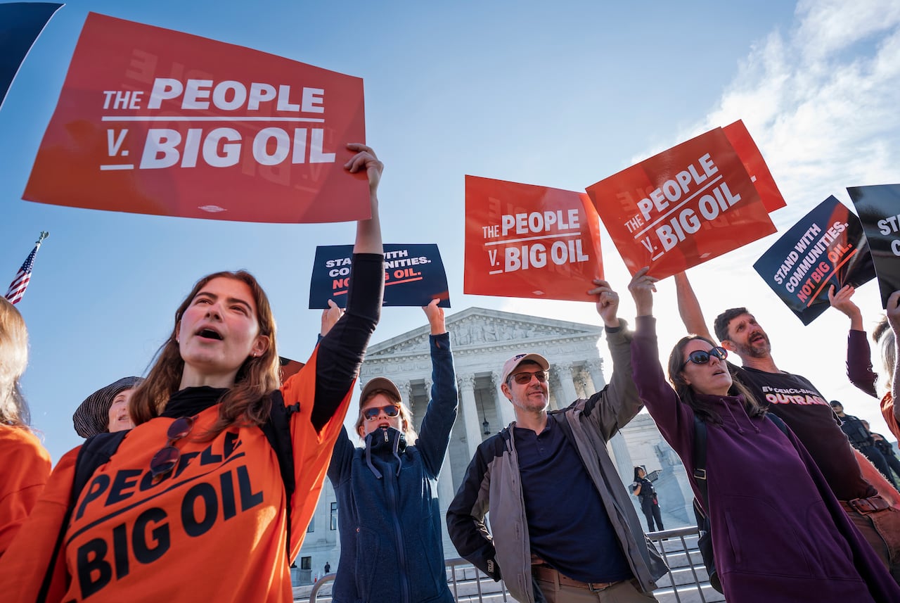 Protesters stand in front of a court holding signs that read 'The people v. Big Oil'