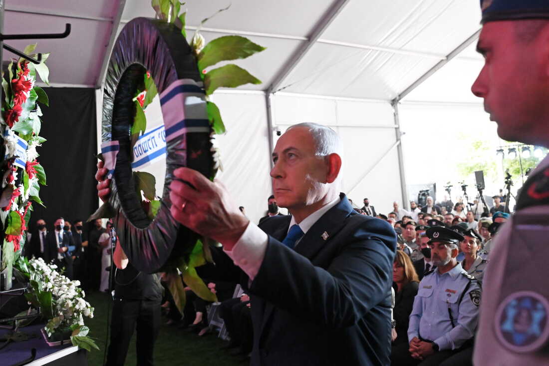 Israeli Prime Minister Benjamin Netanyahu holds up a wreath as he places it during a state memorial ceremony in memory of those killed in the October 7, 2023, Hamas-led attack on Israel, at Mount Herzl cemetery in Jerusalem on October 5. Rows of people are standing behind him.