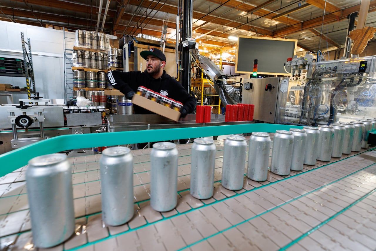 Aluminum cans are seen in a factory with a worker behind them.