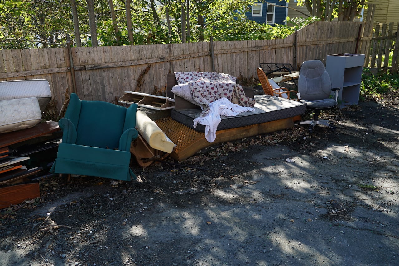 A pile of discarded and dirty furniture next to a fence.