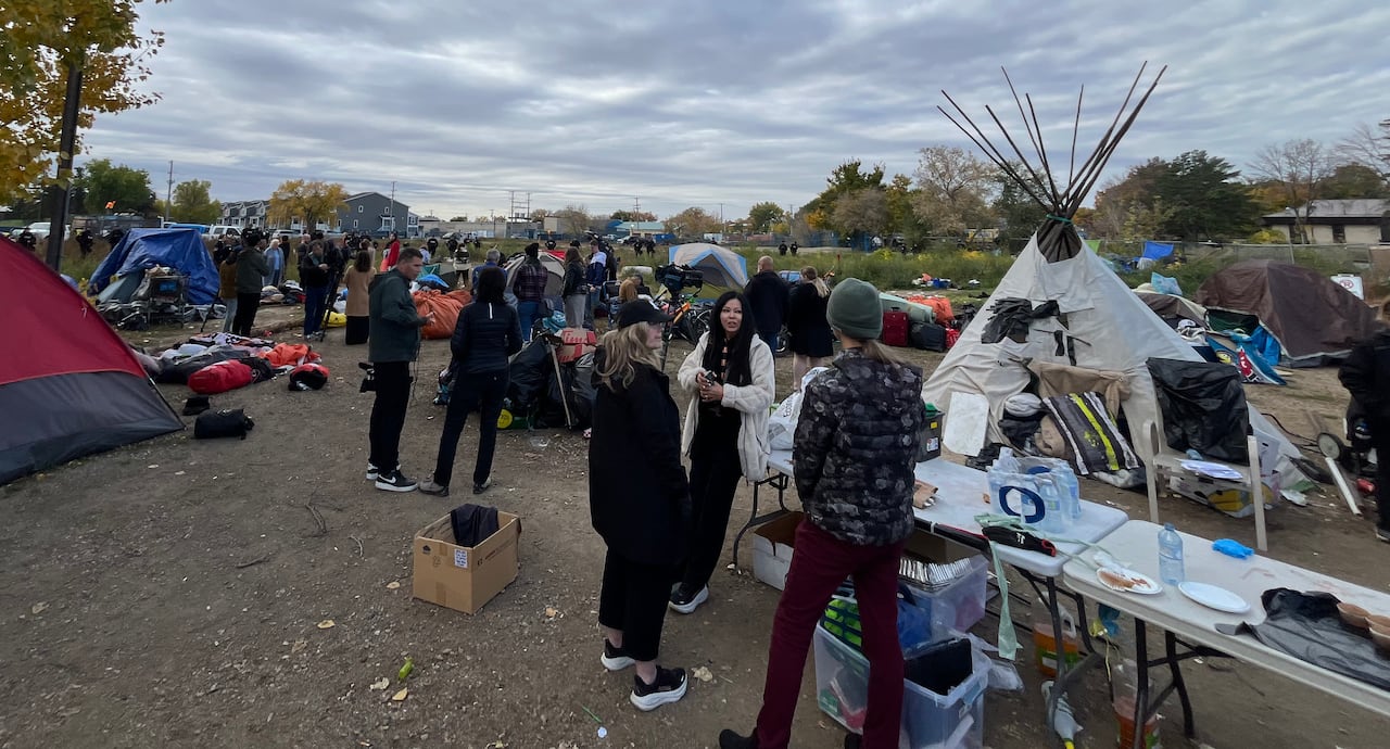 people mill about on an undeveloped plot of land with tents and a teepee