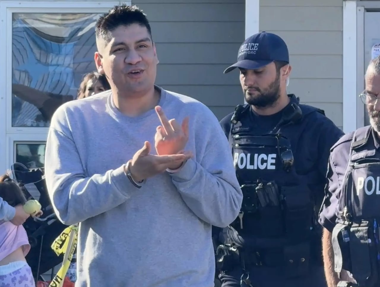 A man makes an obscene gesture at the camera, with two police officers behind him.