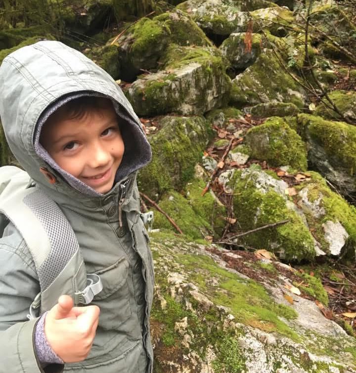A kid in a jacket smiling in a rocky wooded area